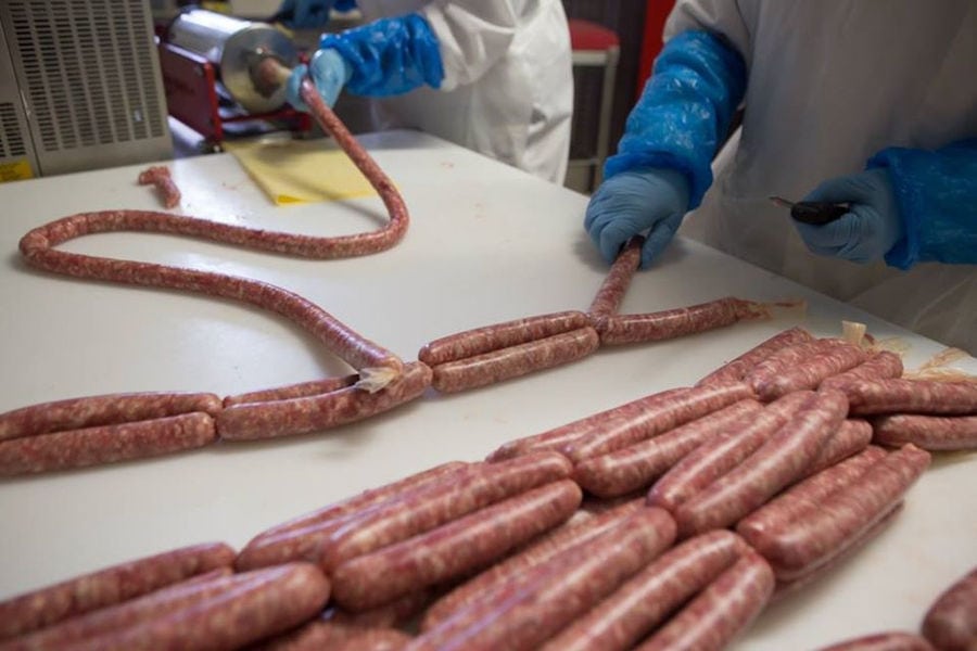 close-up of two men workers at Vavourakis Farm workshop one of them stuffing sausage and the other putting them on white table